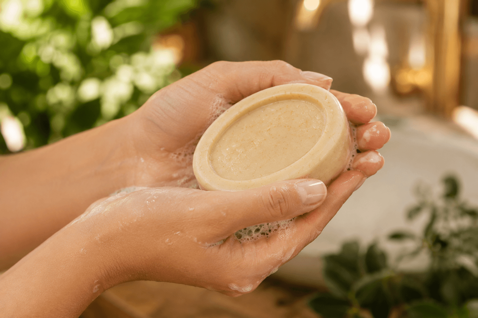 Two hands working a cream soap bar into a rich botanical lather